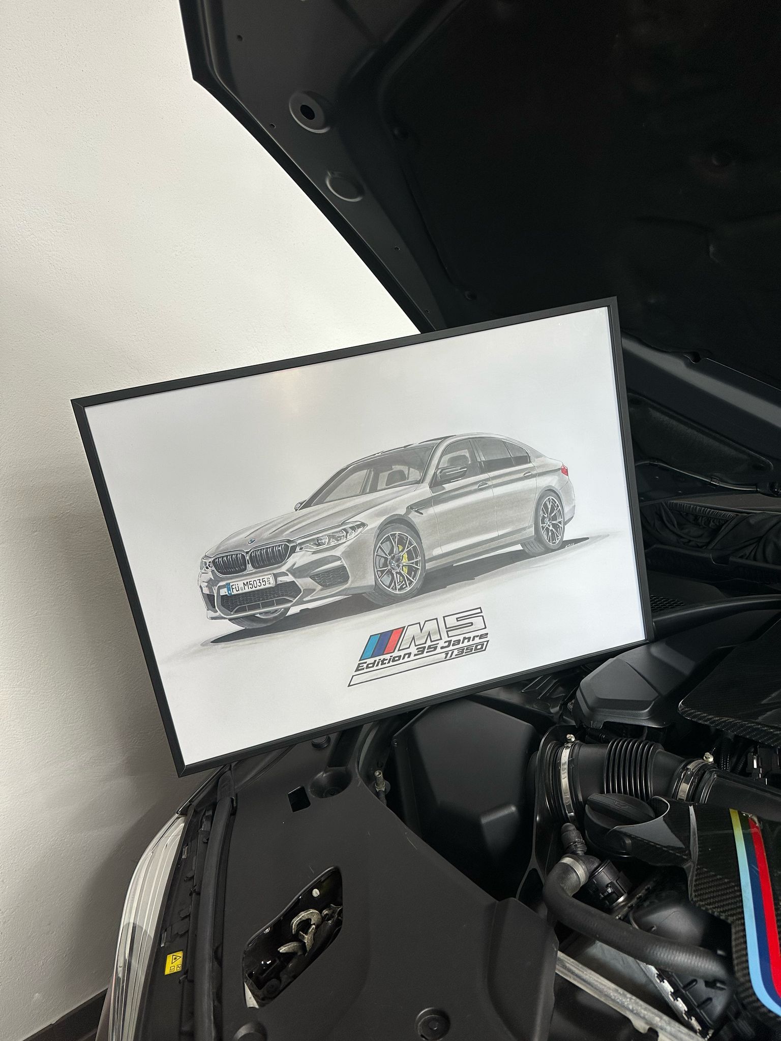 Gerahmtes Bild eines silbernen BMW M5 vor dem geöffneten Motorraum eines Fahrzeugs