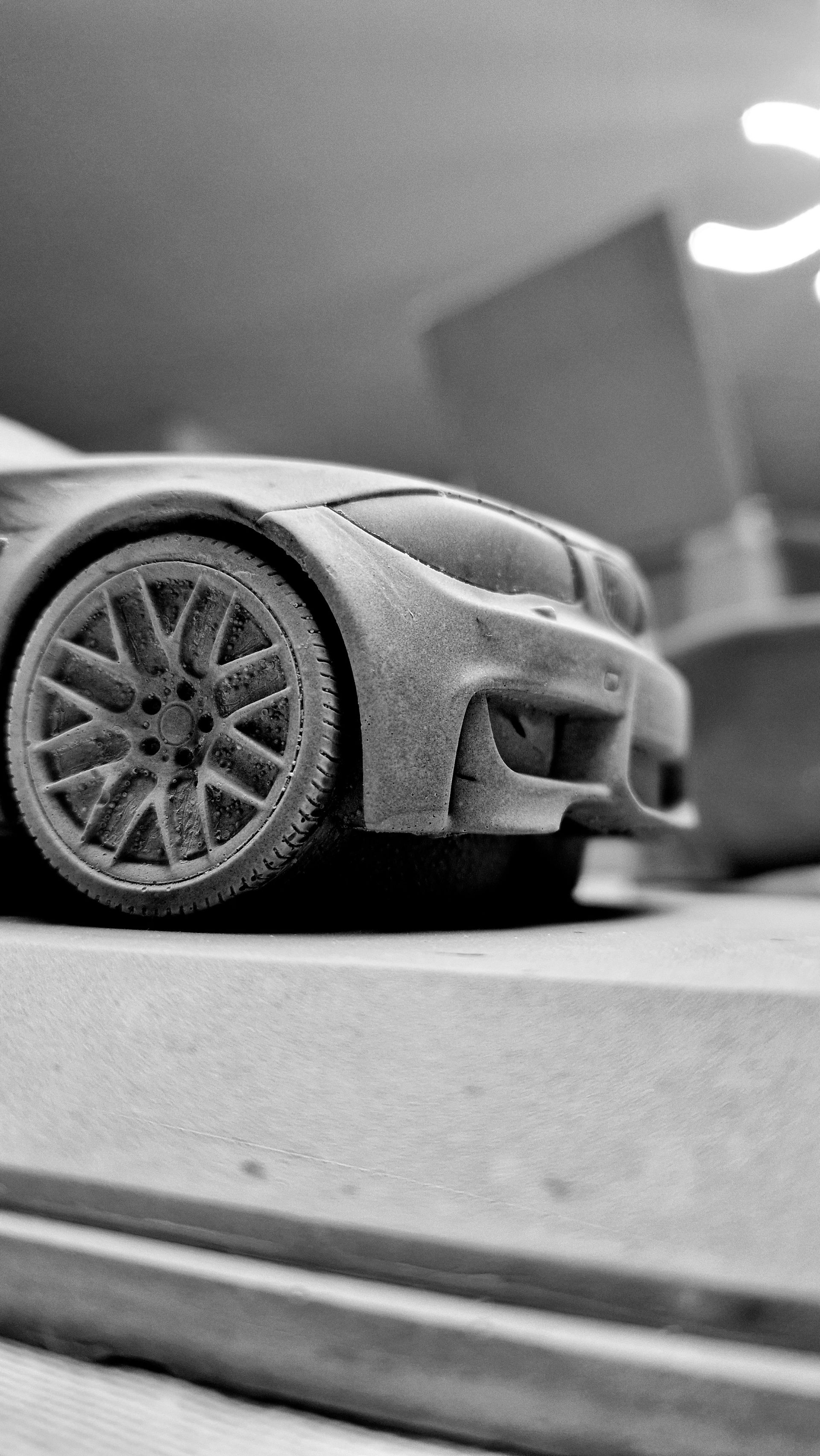 Schwarzweiße Nahaufnahme einer Autoskulptur mit ausgearbeitetem Rad und Frontpartie