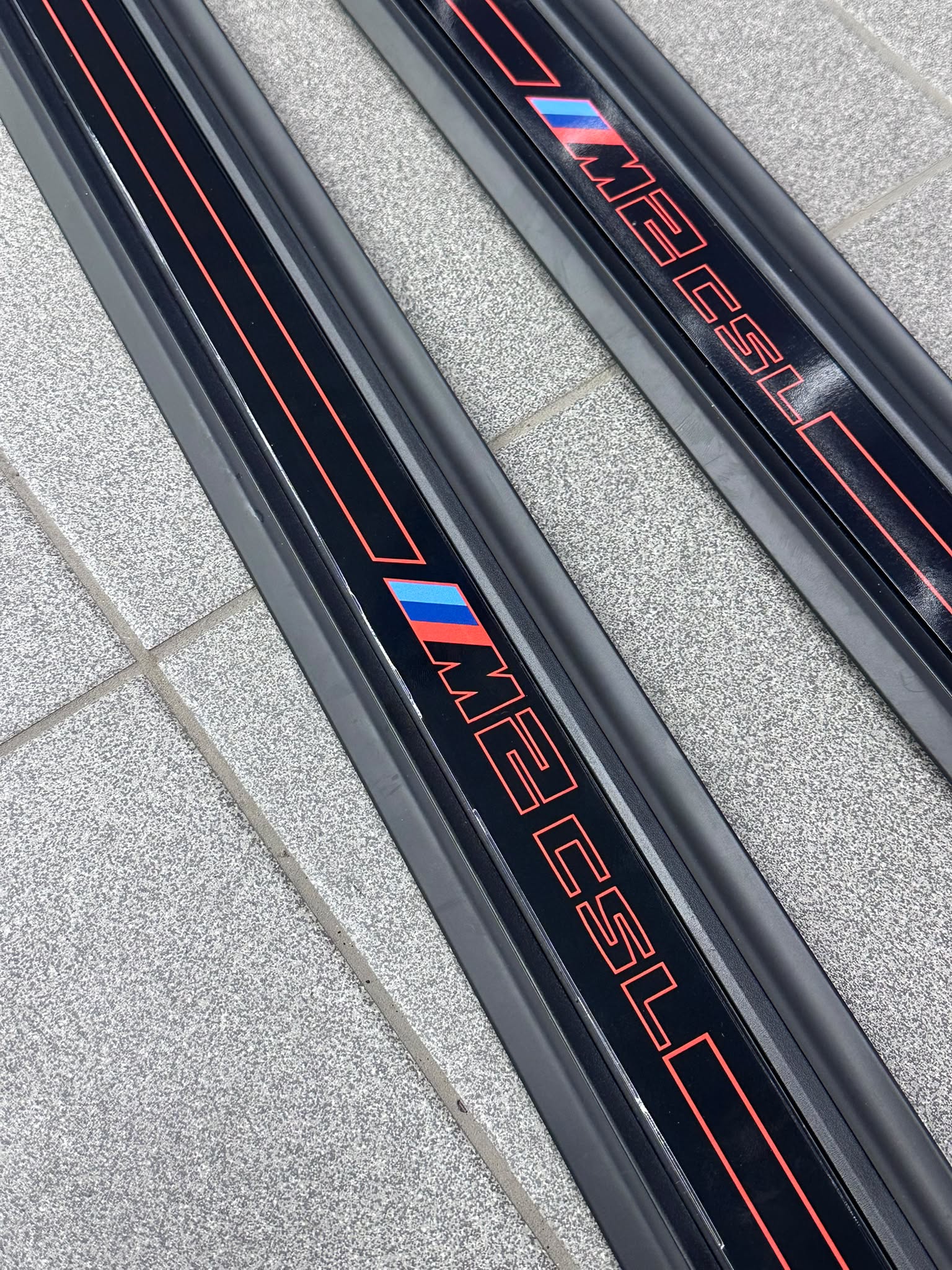 Zwei schwarze BMW-Einstiegsleisten mit roten Konturen und M2-CSL-Schriftzug