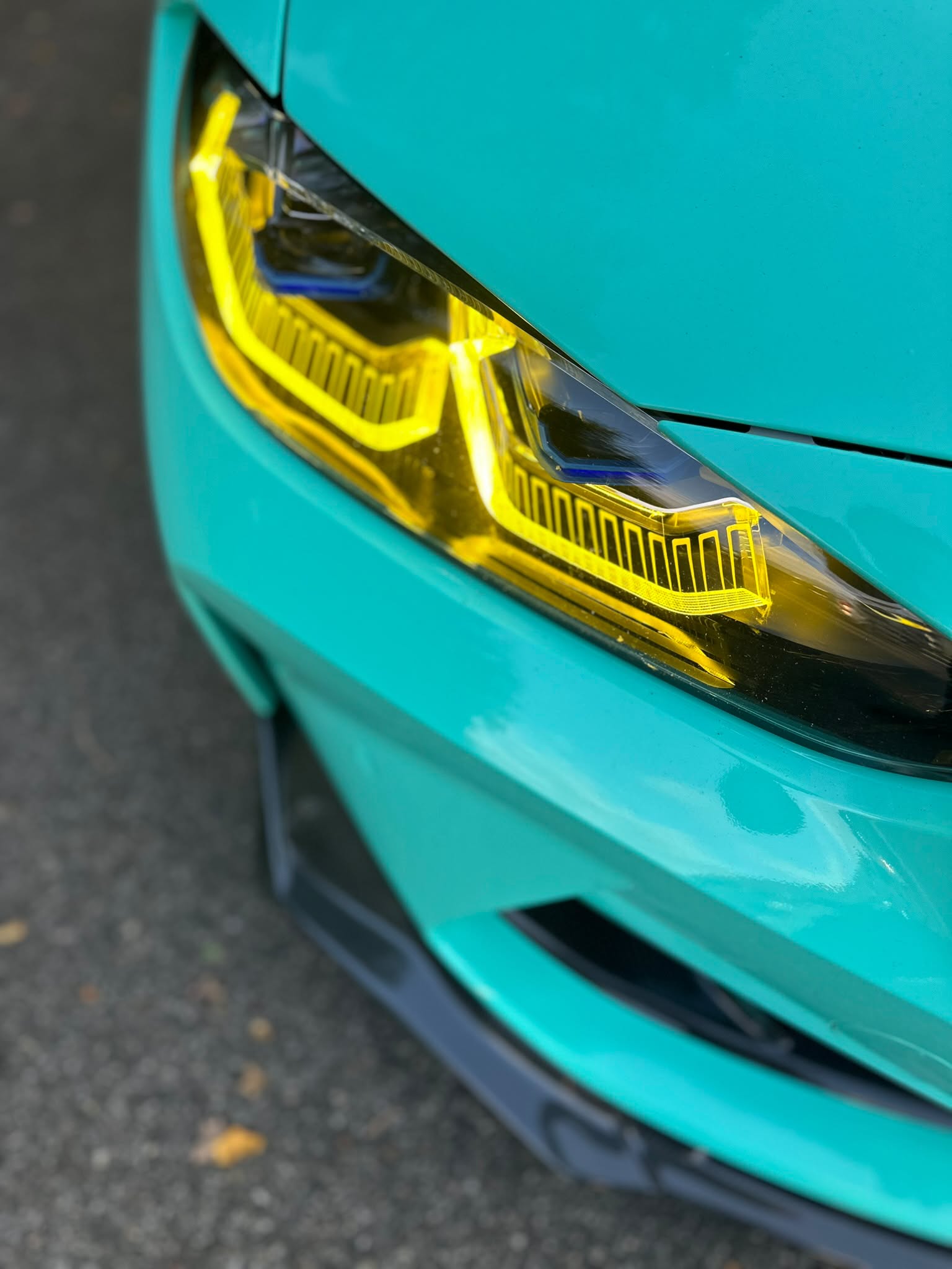 Detail eines BMW-Scheinwerfers mit gelben Lichtakzenten an türkisfarbener Karosserie